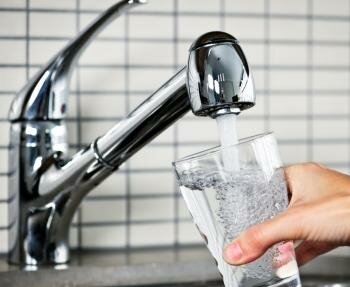  Person füllte ein Glas mit Wasser aus einem Wasserhahn